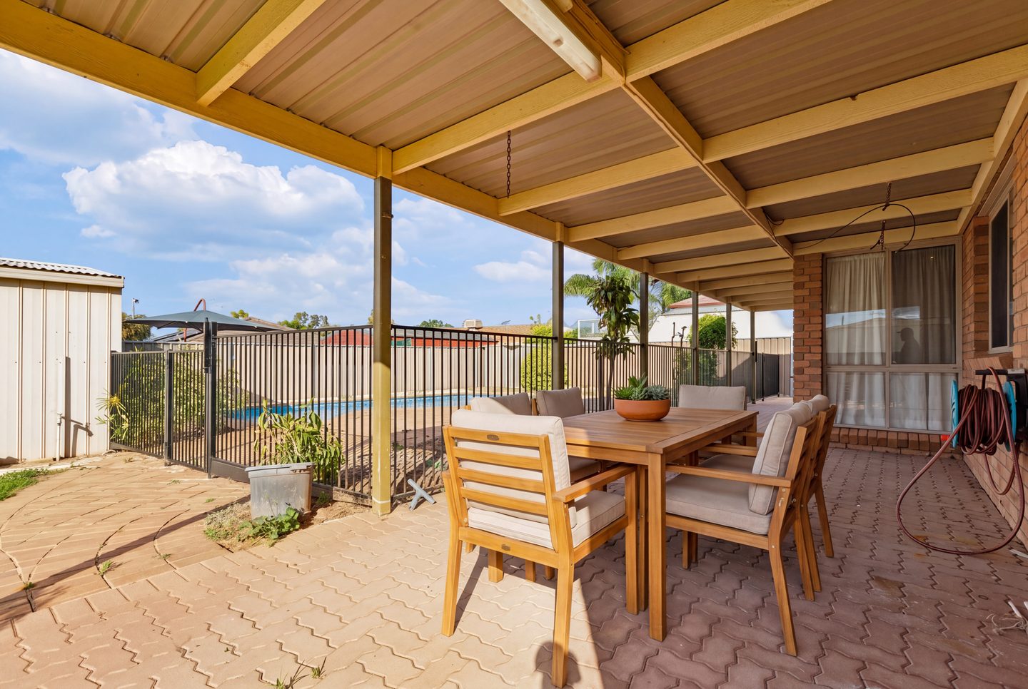 Covered paved entertaining area beside the fenced pool