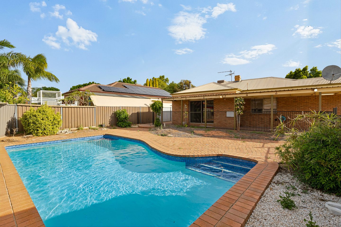 Inground pool with brick paving and the home's covered outdoor area beyond