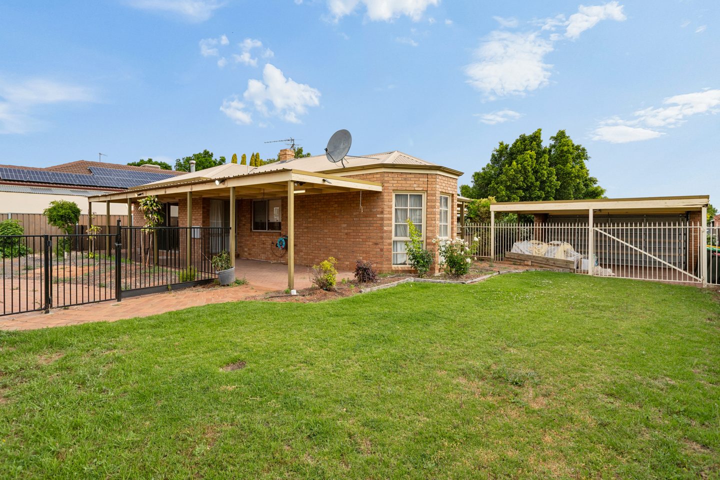 Lawn beside the brick home, with the pool fence and carport visible